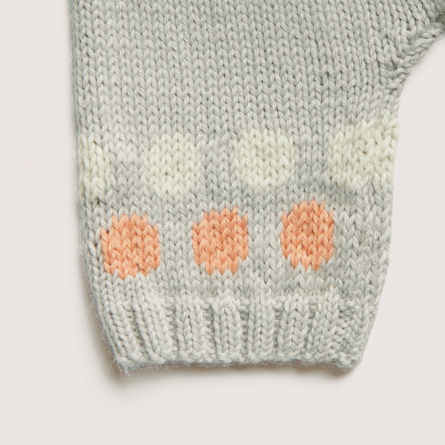 Rico Baby 042: Gestrickter Ärmel in Silbergrau mit apricotfarbenen und salbeifarbenen Punkten.