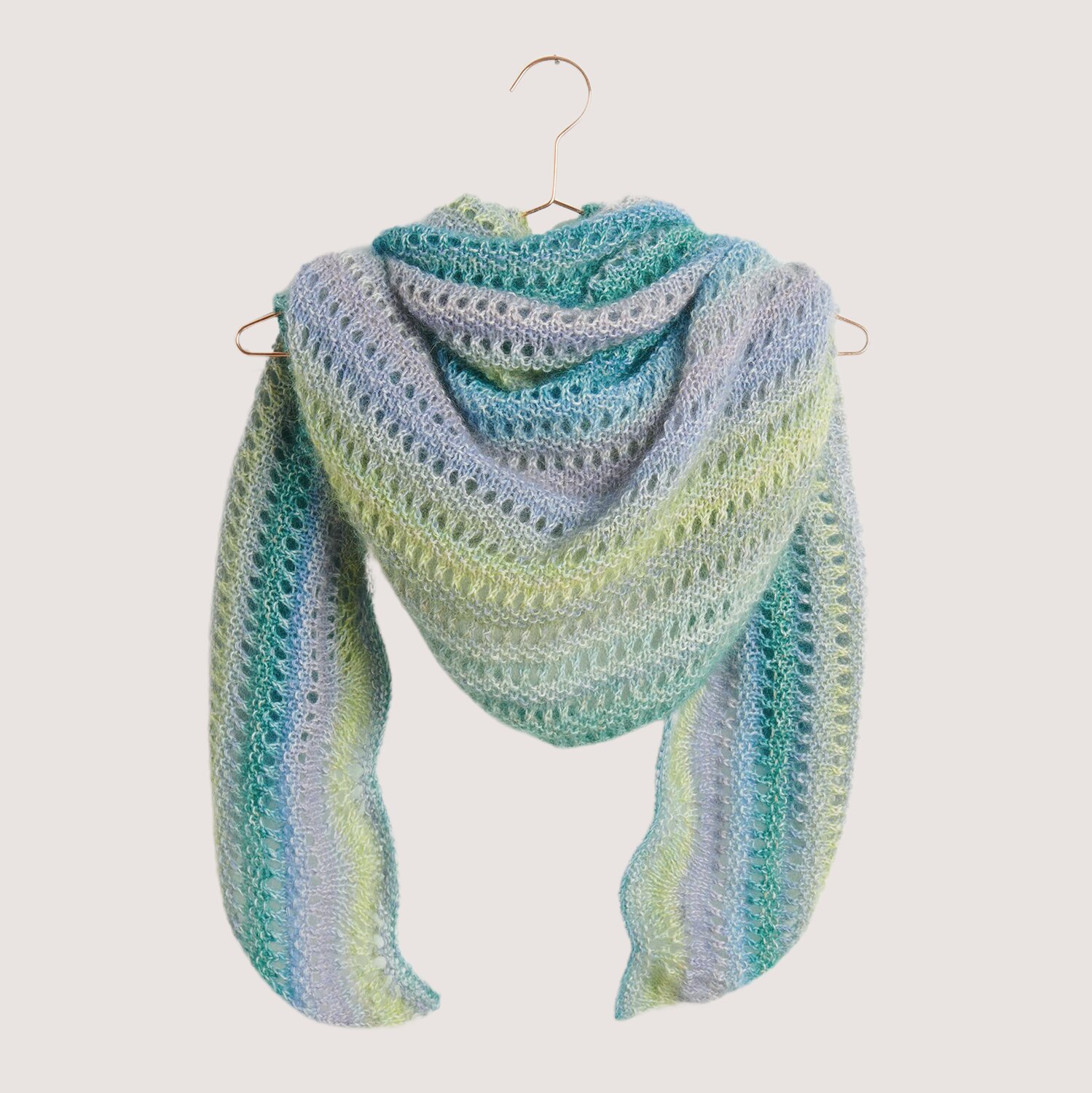 Strickset Dreieckstuch Modell 06 doppelfädig aus Die Neue Masche Nr. 9 von idee. Creativmarkt Strickset Dreieckstuch Modell 06 in sanften Pastelltönen, doppelfädig gestrickt, präsentiert auf einem Kleiderbügel.