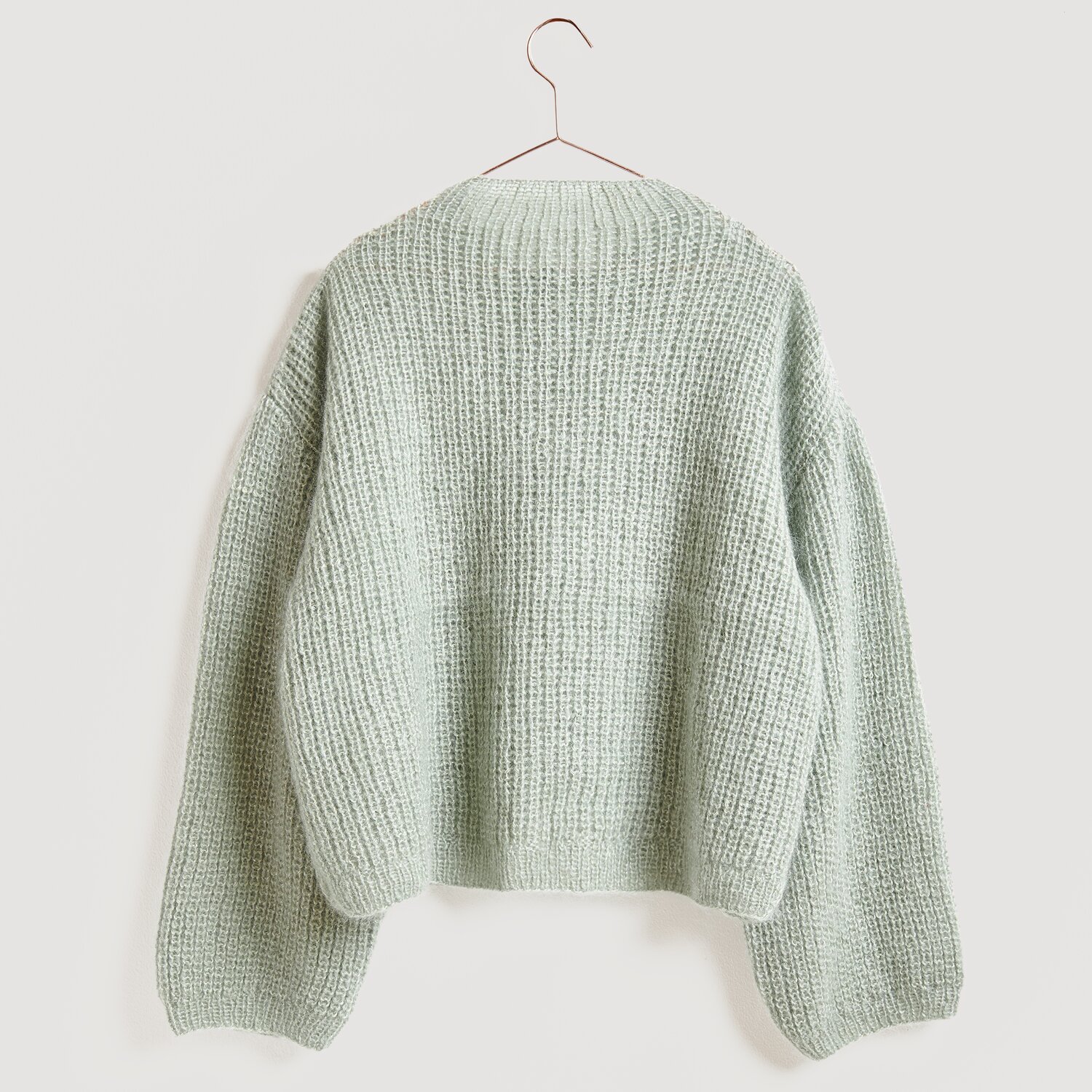 Die Neue Masche No. 13 Herbst von idee. Creativmarkt Essentials Super Kid Mohair Loves Silk Glamorous Glitter Pullover in sanftem Efeu-Grün, präsentiert auf einem Kleiderbügel.