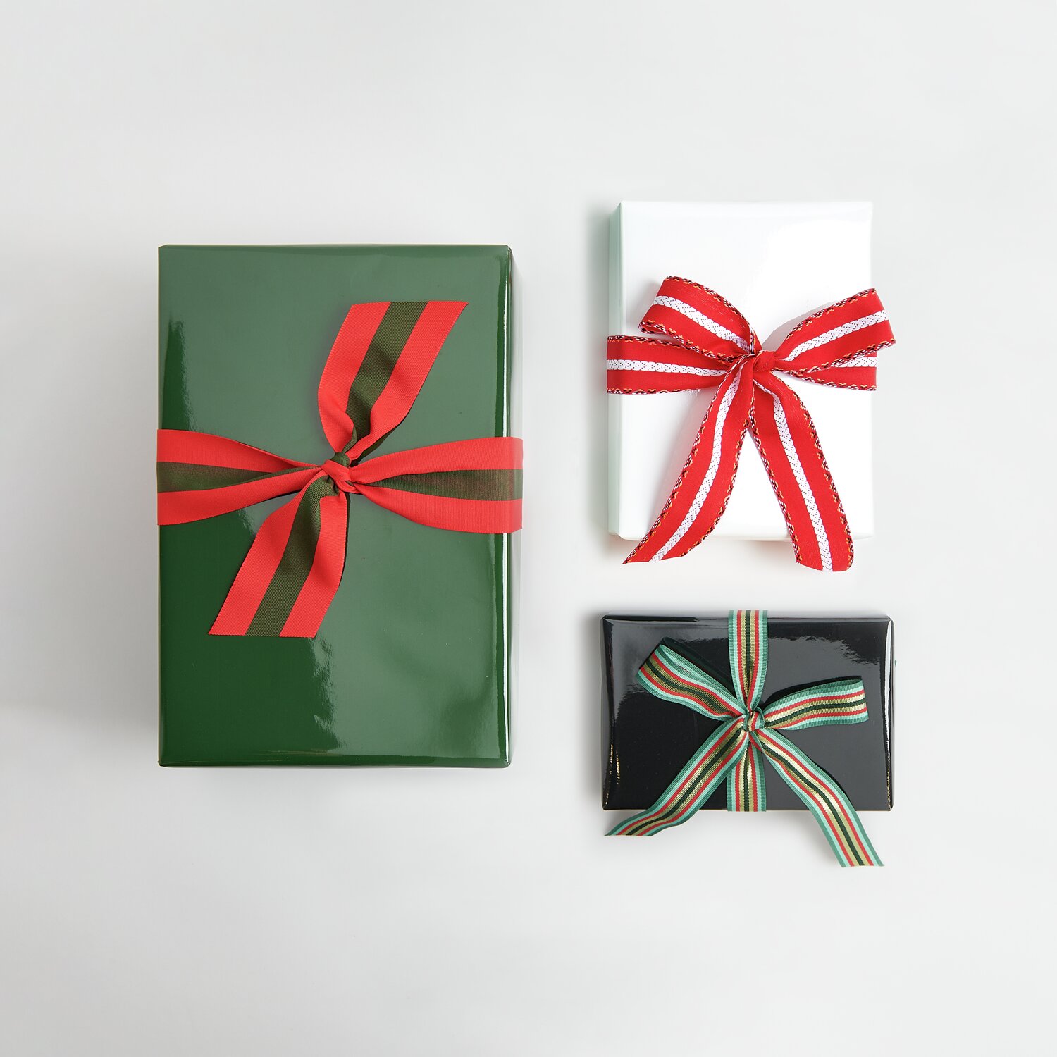 Paper Poetry Geschenkpapier Lack Schwarz/Grün/Weiß Mix, drei Geschenke mit roten und gestreiften Bändern dekoriert.