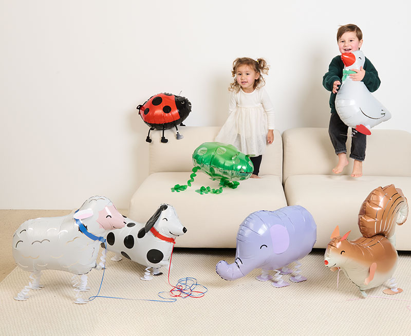 Zwei Kinder stehen auf einem Sofa mit vielen Folienballons in Tierform aus der Kollektion Rico Chingus.