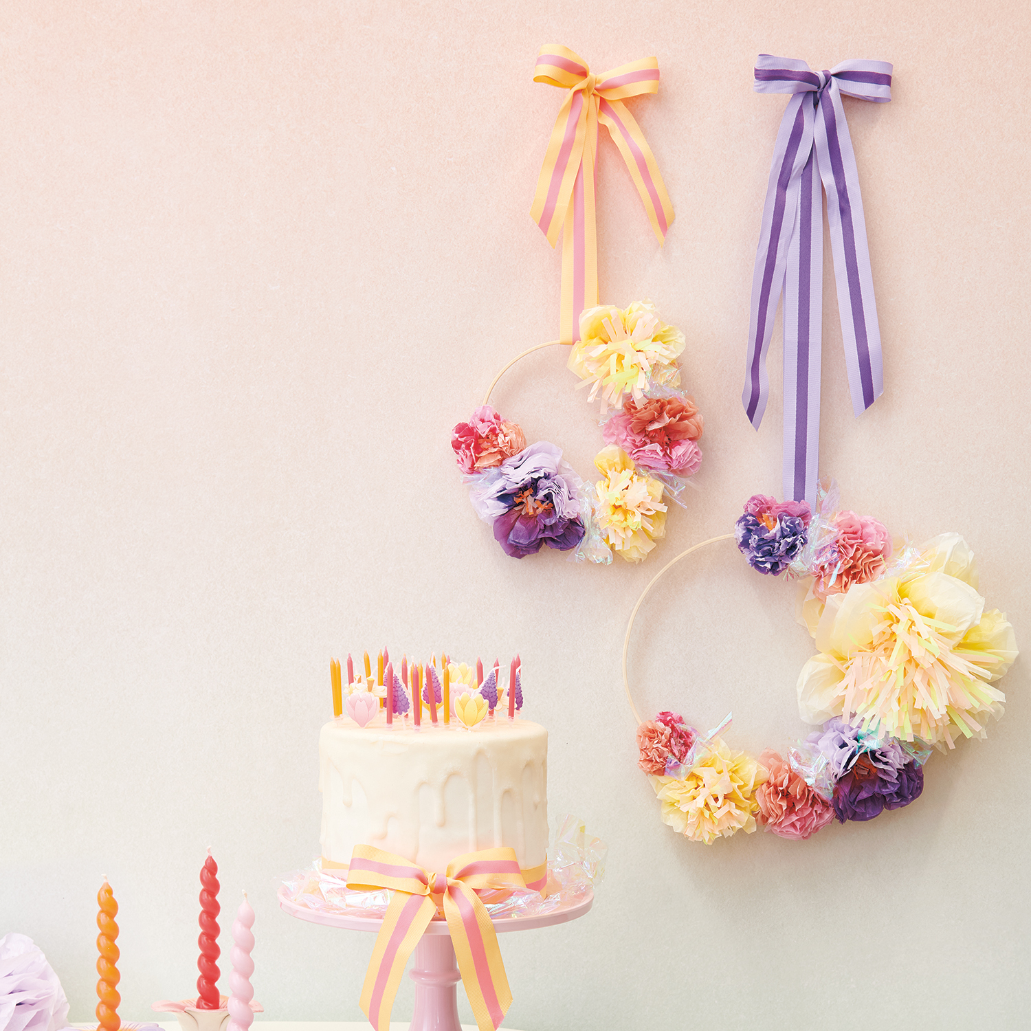 Bastelanleitung Dekoring mit Seidenpapierblumen: Zwei bunte Dekoringe mit Schleifen an der Wand, darunter eine verzierte Torte.