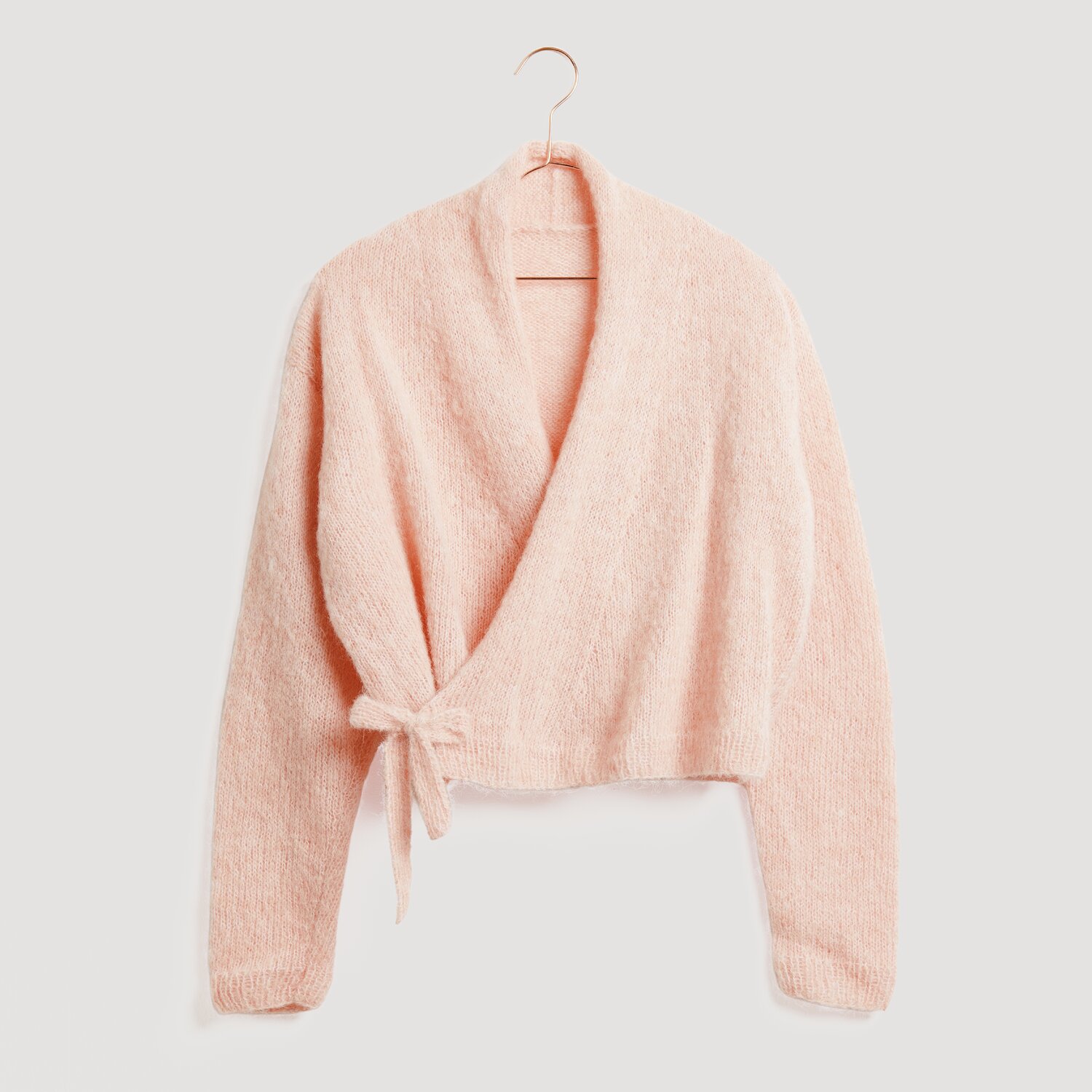 Lovewool No. 21 Herbst-Winter Sprachauswahl deutsch von Rico Design Weiches, rosa Wickeloberteil von Modell Legeware, auf einem Kleiderbügel präsentiert. Ideal für gemütliche Anlässe, vereint es Stil und Komfort in einem eleganten Design.