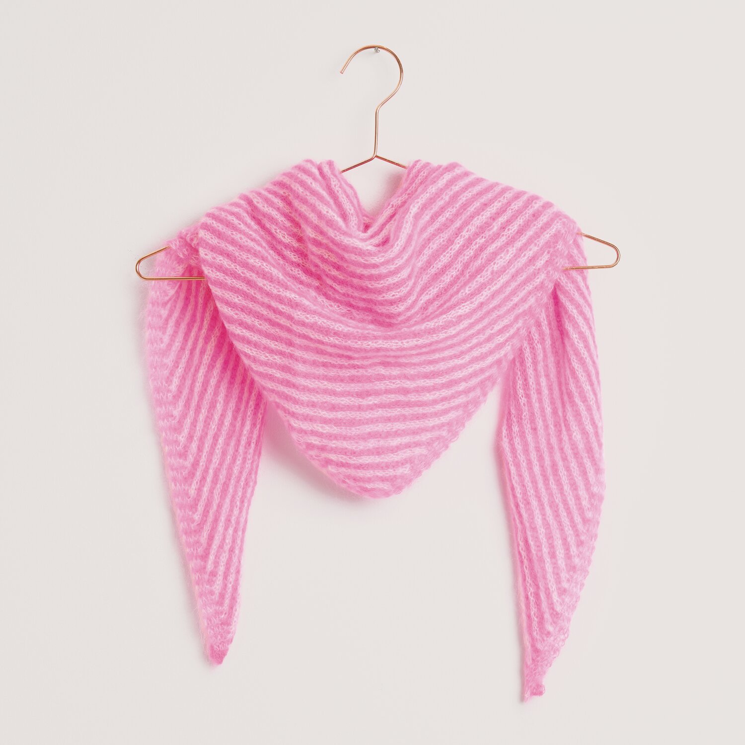 Essentials Super Kid Mohair Loves Silk 25g 200m Farbe Weiß von Rico Design Strickset Dreieckstuch Modell 33 aus Made by Me Nr. 18, gestrickt in Weiß und Neon-Pink, hängt auf einem Kleiderbügel.