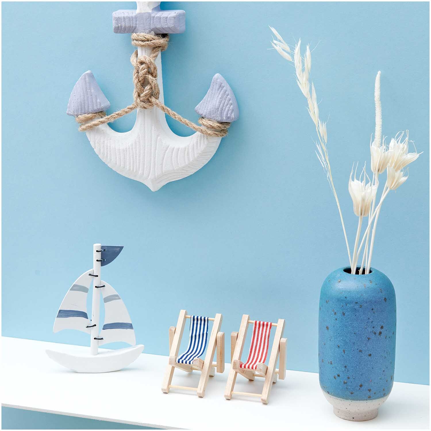 Deko-Liegestuhl blau-weiß vor maritimer Kulisse mit Anker, Segelboot und blauer Vase.
