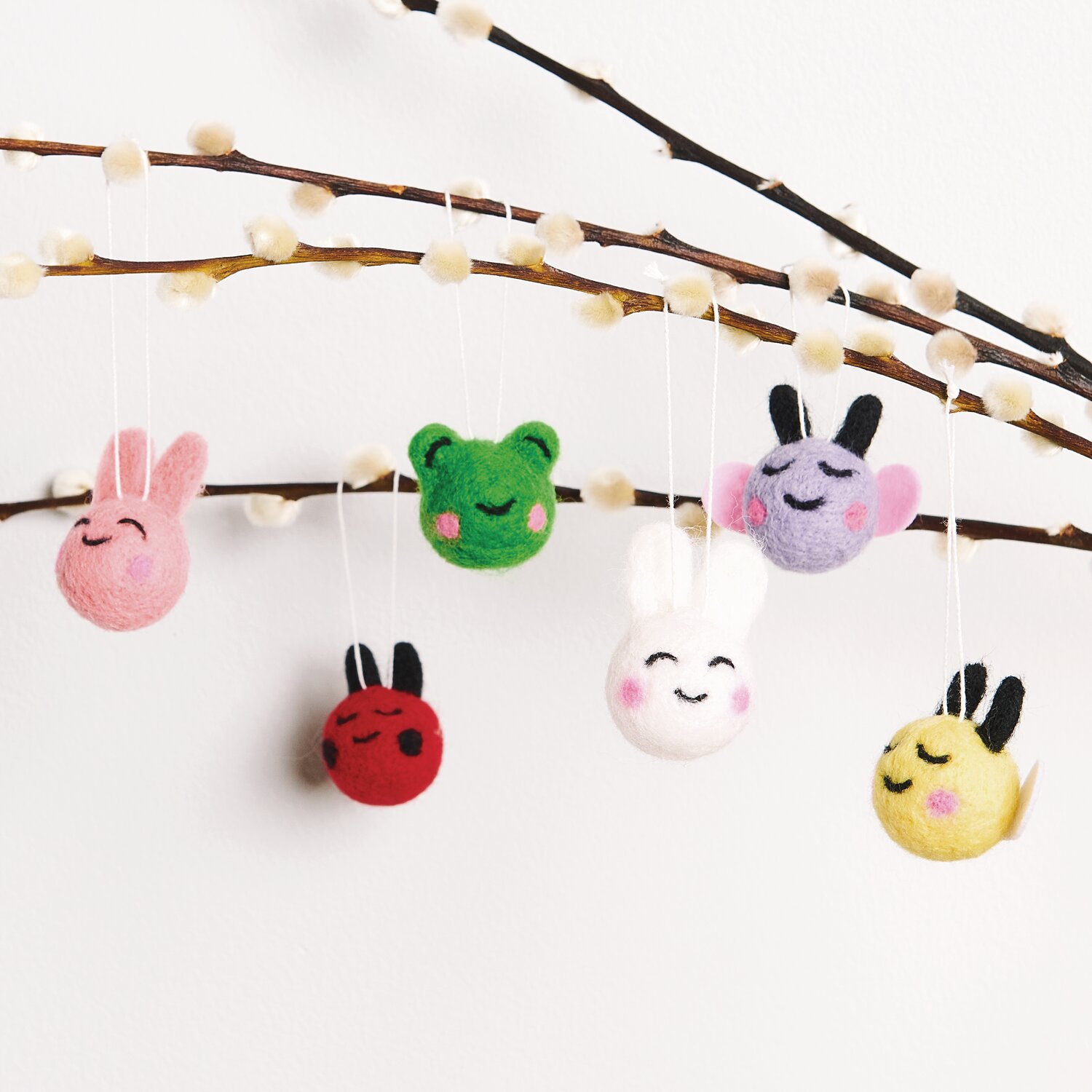 Aufhänger Filz-Köpfe 3D Bunt: Sechs bunte Filzfiguren hängen an Zweigen, ideal für kreative Dekorationen.