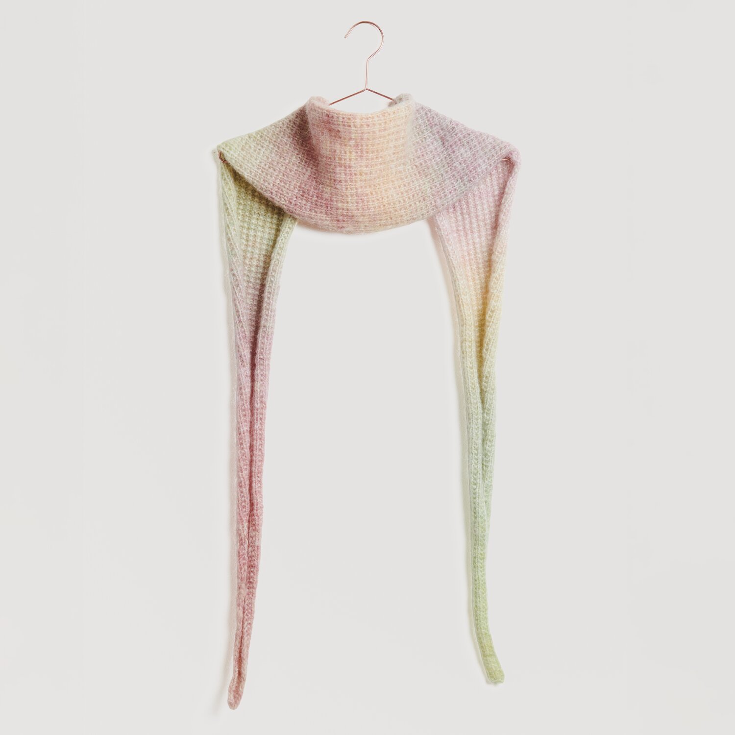 Lovewool No. 21 Herbst-Winter Sprachauswahl deutsch von Rico Design Ein langer, gestrickter Schal in sanften Pastelltönen hängt an einem Haken. Der Schal zeigt einen Farbverlauf von Rosa zu Grün. Marke: Modell Legeware. Ideal für stilvolle Wintermode.