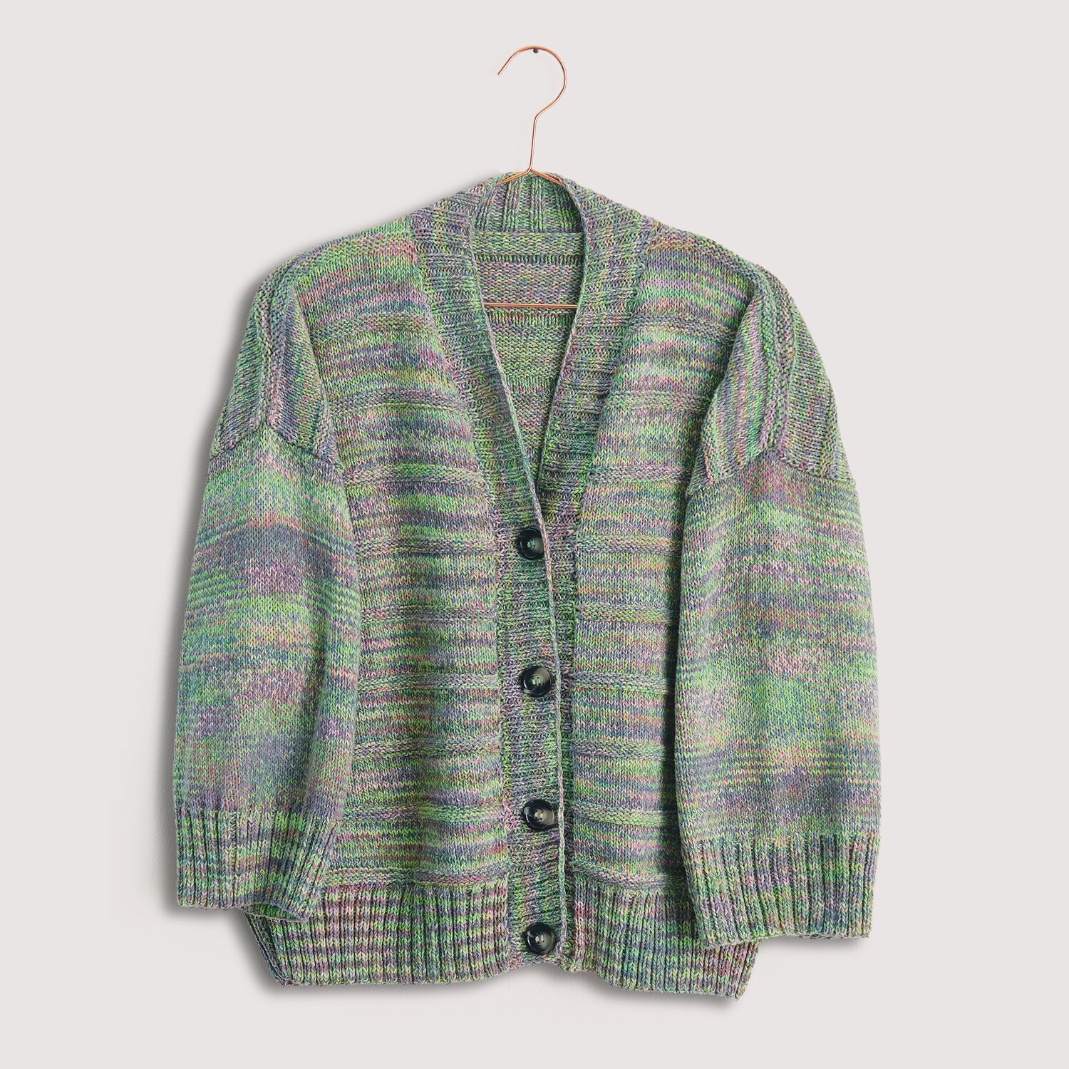 Die Neue Masche No. 12 Frühjahr-Sommer von idee. Creativmarkt Strickset Jacke Modell 19 aus Die Neue Masche No. 12, gestrickt in grünen und lila Tönen, präsentiert auf einem Kleiderbügel.