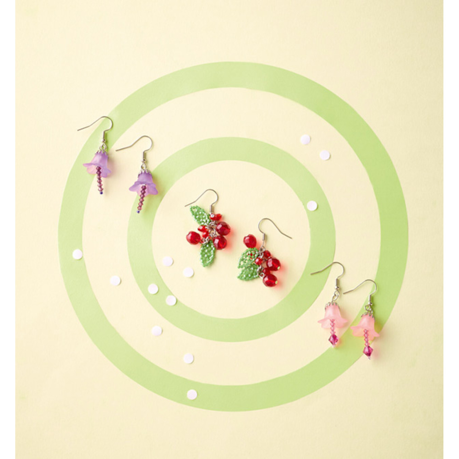 Schmuck aus Miniperlen: Drei Paar Ohrringe in Lila, Rot und Rosa auf grünem, kreisförmigem Hintergrund.