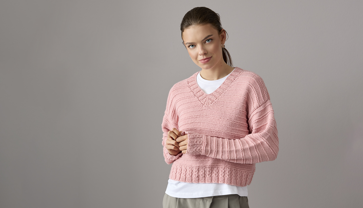 Strickanleitung Pullover aus Essentials Vegan Cashmere aran Strickanleitung Pullover aus Essentials Vegan Cashmere aran: Frau trägt rosa V-Pullover.
