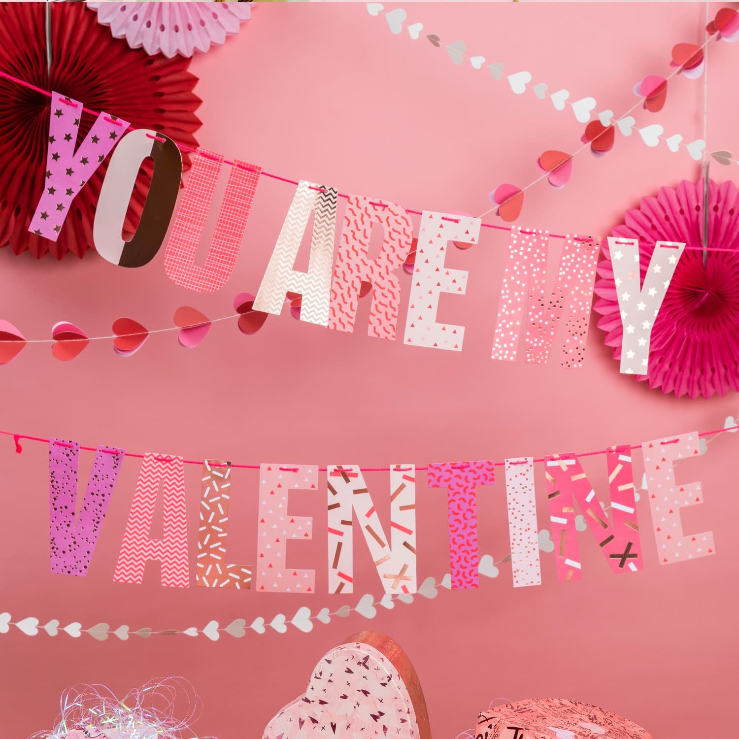 Pinke Girlanden mit dem Schriftzug „YOU ARE MY VALENTINE“, dahinter weitere Herz-Girlanden und hängende Fächer. Fotosetting pinke Wand.