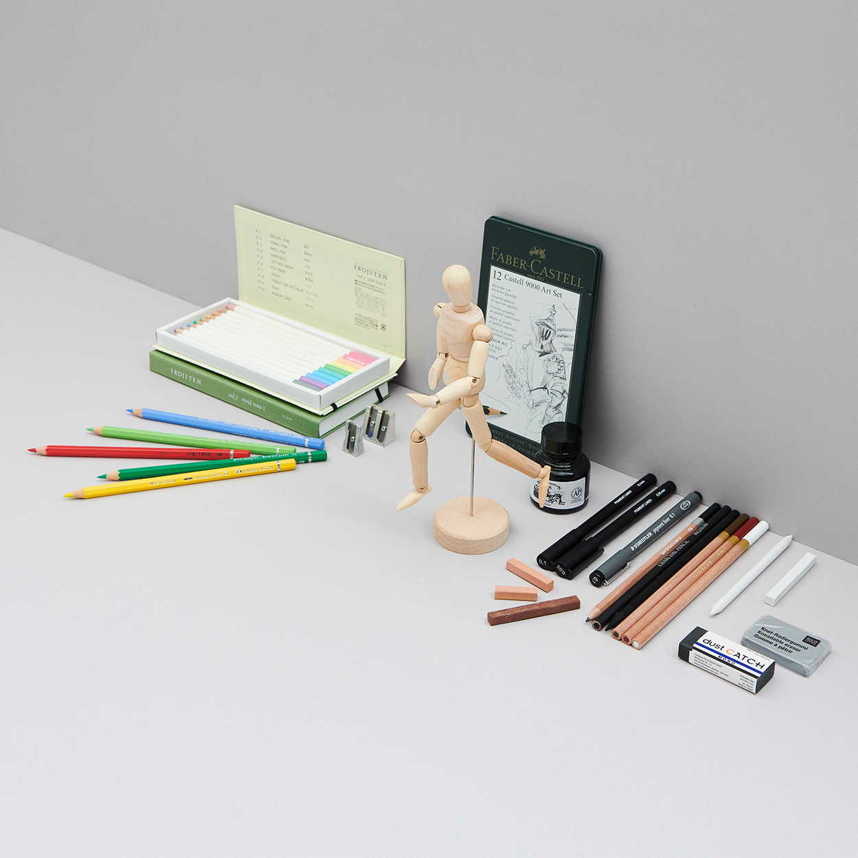 Blei- und Buntstifte mit Radiergummi, Metall Etui und Modellpuppe. Fotosetting graue Ecke.
