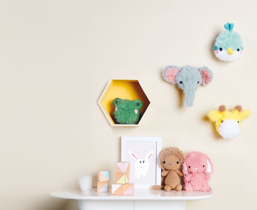 Verschiedene Ricorumi-Häkeltiere hängen an der Wand und sitzen auf einem Tisch