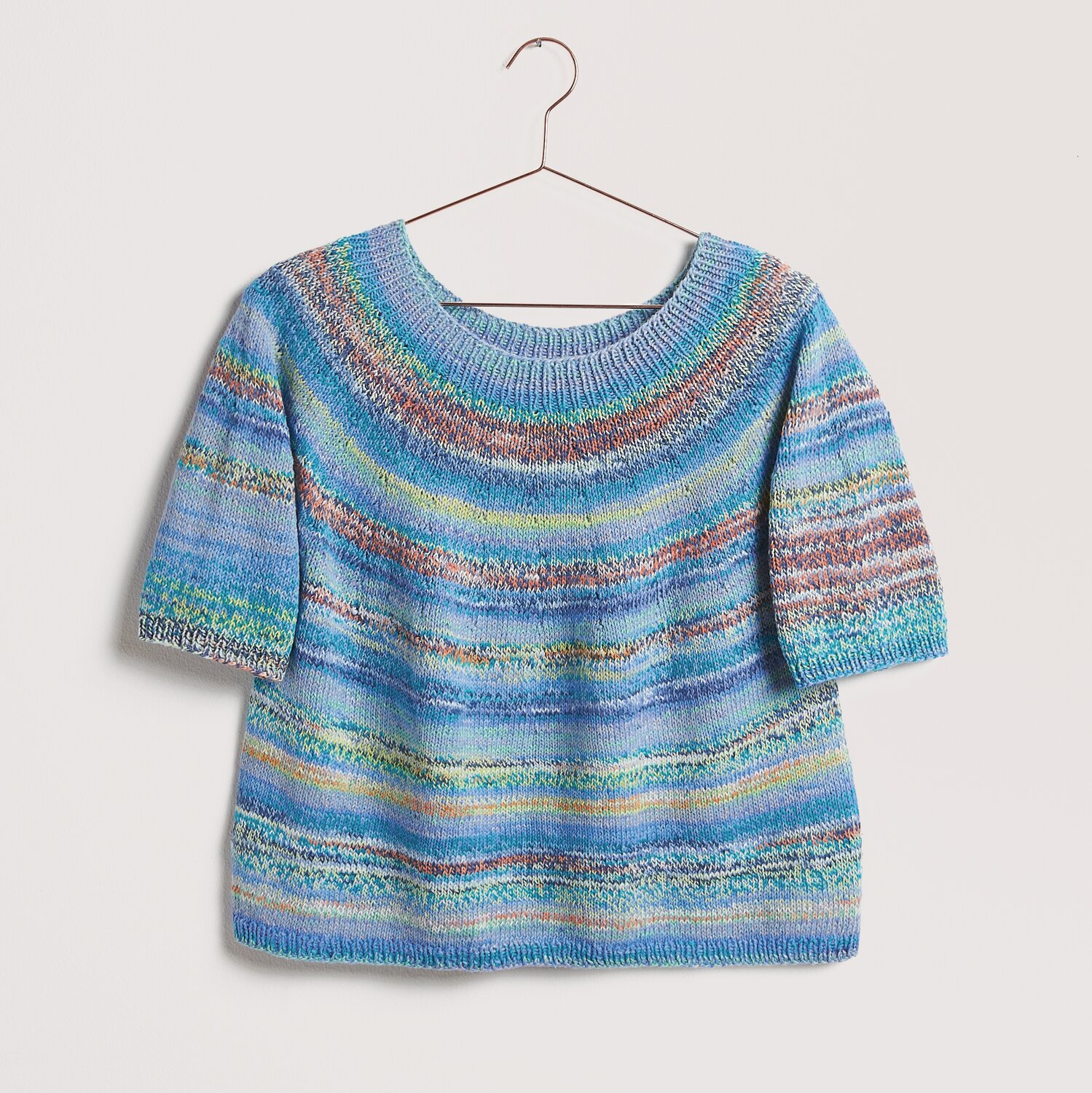 Die Neue Masche No. 12 Frühjahr-Sommer von idee. Creativmarkt Strickset Shirt Modell 22 aus Die Neue Masche No. 12, blau gestreift, auf einem Kleiderbügel.