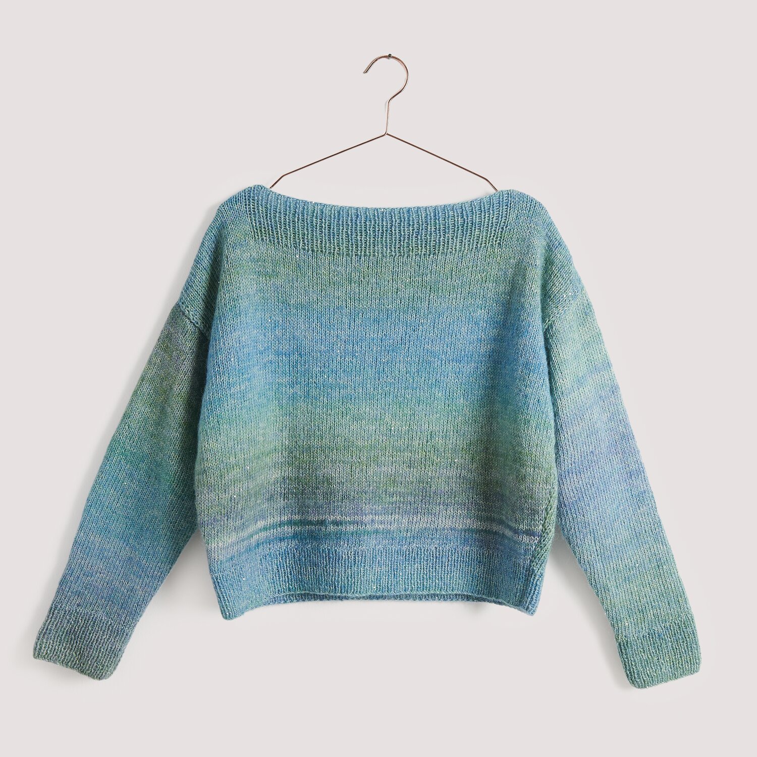 Strickset Pullover Modell 28 aus Die Neue Masche No. 15, in Blau- und Grüntönen, auf einem Kleiderbügel vor neutralem Hintergrund.