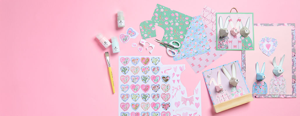 Gebastelte Osterhasen und Bastelpapier in verschiedenen Farben und Mustern und Acrylfarben mit Pinsel. Flatlay von Produkten.