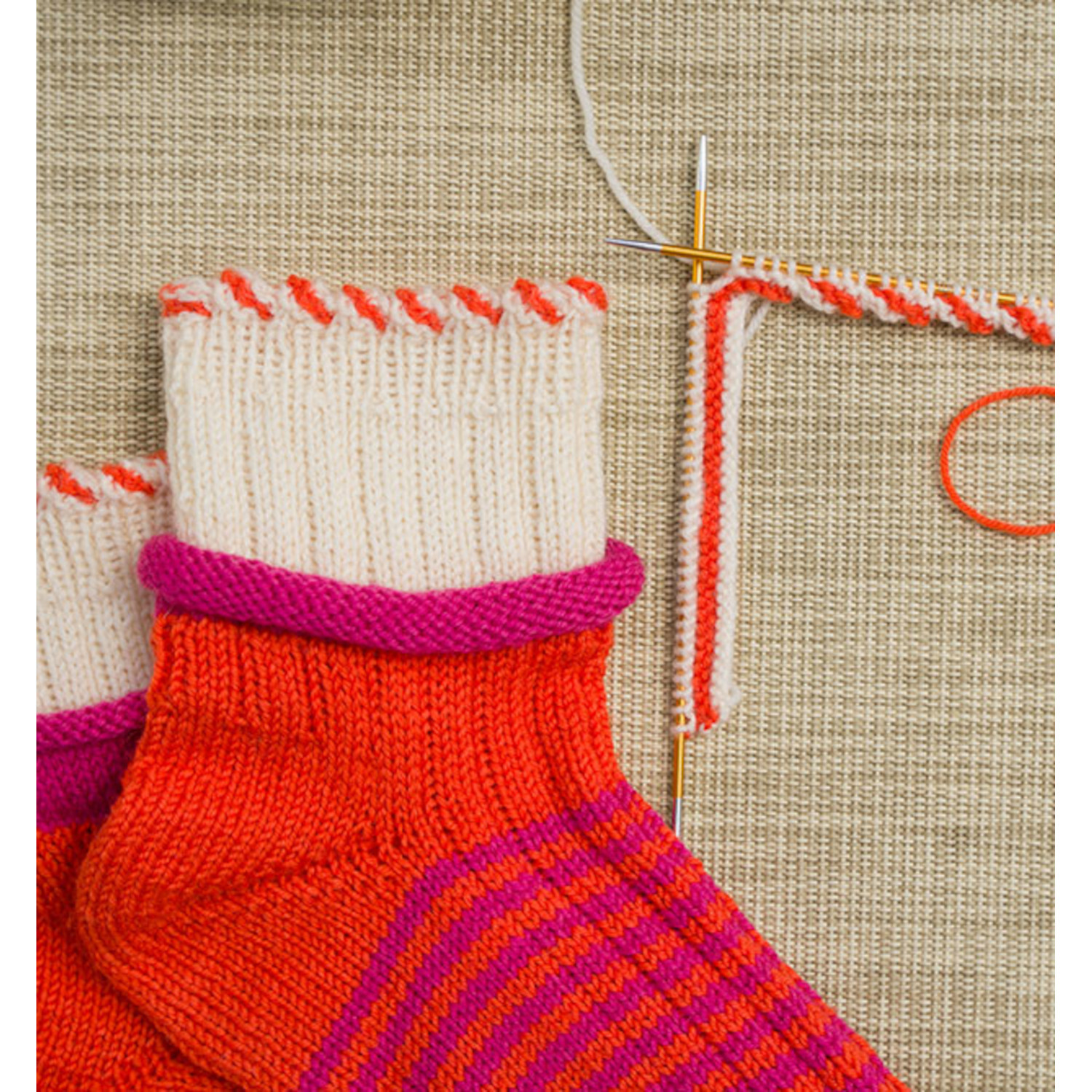 Sockenliebe Tanja Steinbach: Bunte gestrickte Socken in Rot und Pink auf beigem Hintergrund.