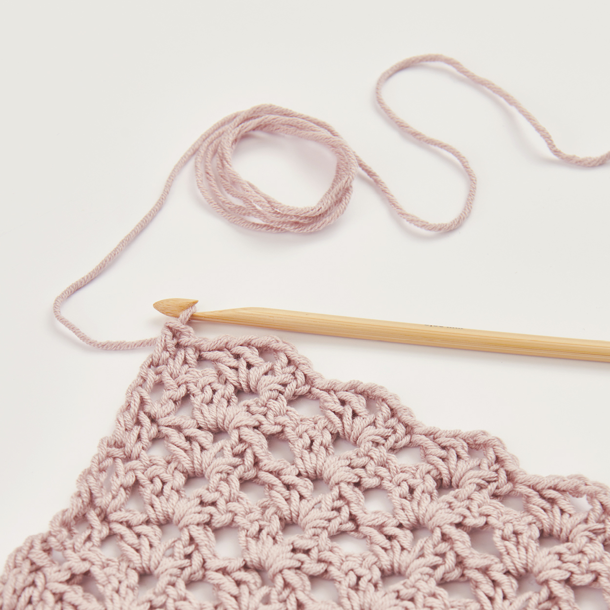 Häkelnadel an einem Häkelstück mit aus rosa Garn. Flatlay von Produkten.