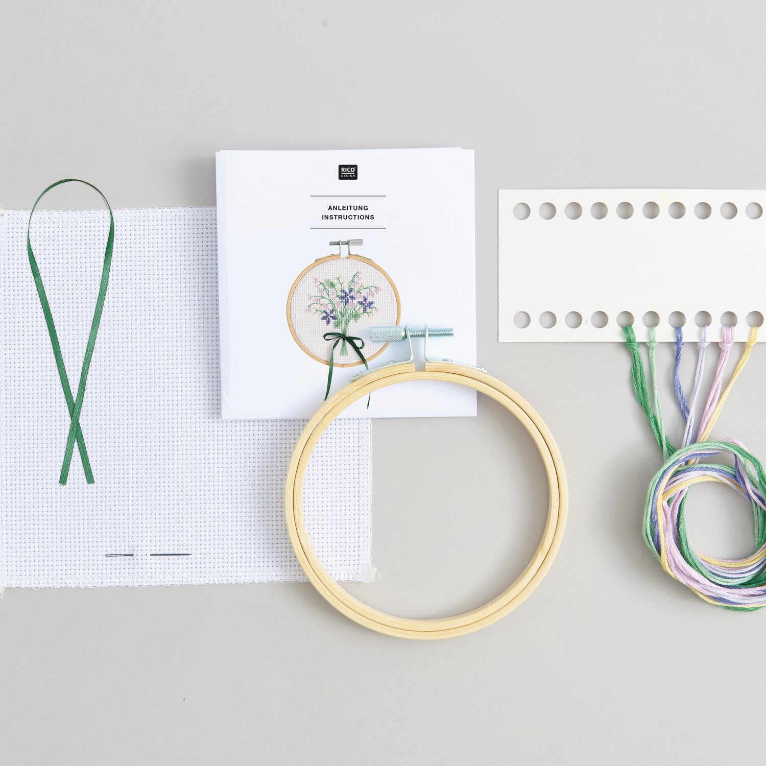 Stickpackung Gezählter Kreuzstich Blumenstrauß mit Stickrahmen, Garn und Anleitung von Rico Design auf grauem Hintergrund.