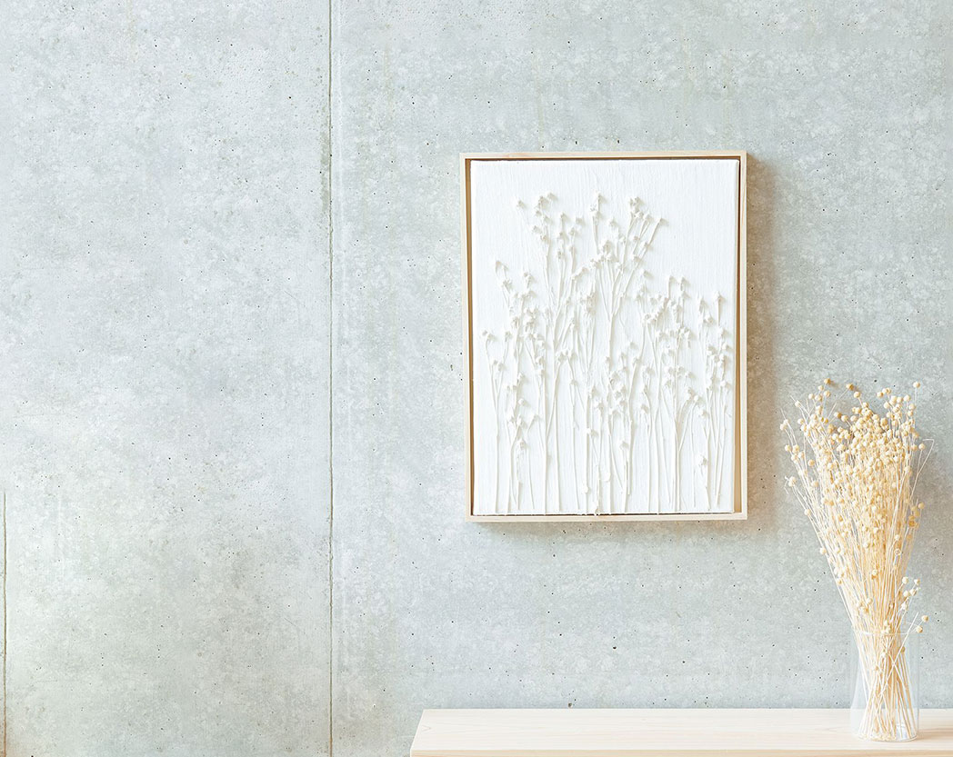 Ein Bild, mit Strukturpaste und Trockenblumen gestaltet, hängt an einer Wand über einem Regal mit Trockenblumen in einer Vase.