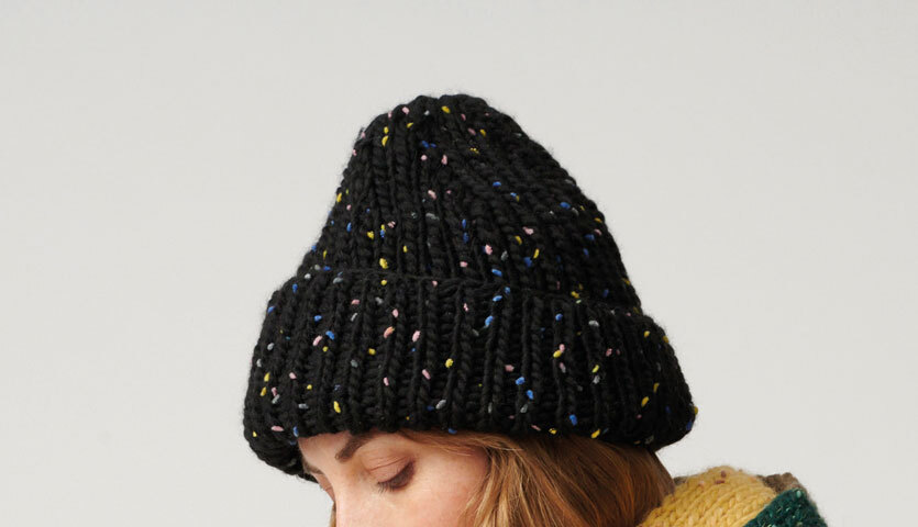 Strickanleitung Creative Jazz Up Mütze: Frau trägt eine schwarze, gestrickte Mütze mit bunten Sprenkeln.