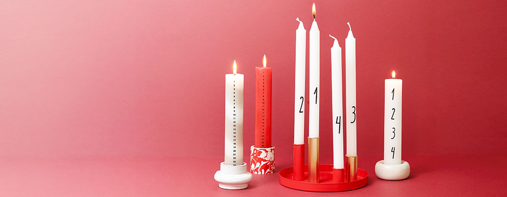 Verschiedenen Adventskalender- und Adventskerzen in verschiedenen Kerzenhaltern. Fotosetting roter Hintergrund.