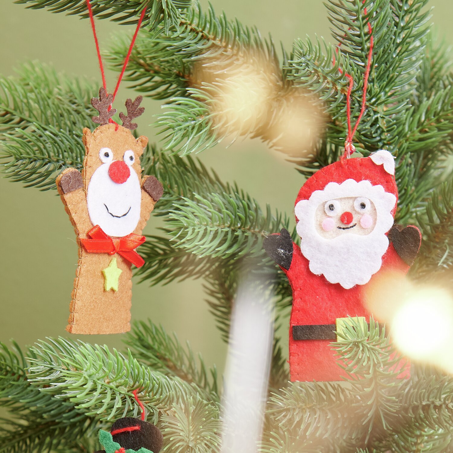 Aufhänger Filz-Rentier flach Braun und Filz-Weihnachtsmann flach Rot von Rico Design an einem Tannenbaum.