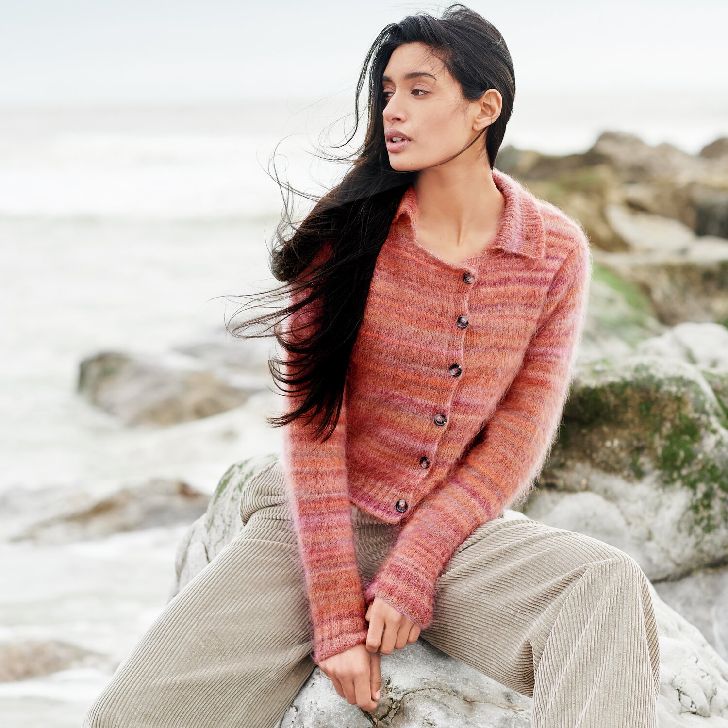 Strickset Jacke Modell 40 aus Lovewool No. 21 von Rico Design Strickset Jacke Modell 40: Frau trägt eine rotbraune Strickjacke am Strand, kombiniert mit beigen Cordhosen.