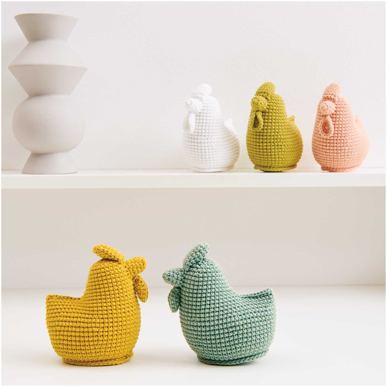 Creative Ricorumi dk: Gehäkelte Hühner in verschiedenen Farben auf einem Regal, dekorativ arrangiert.