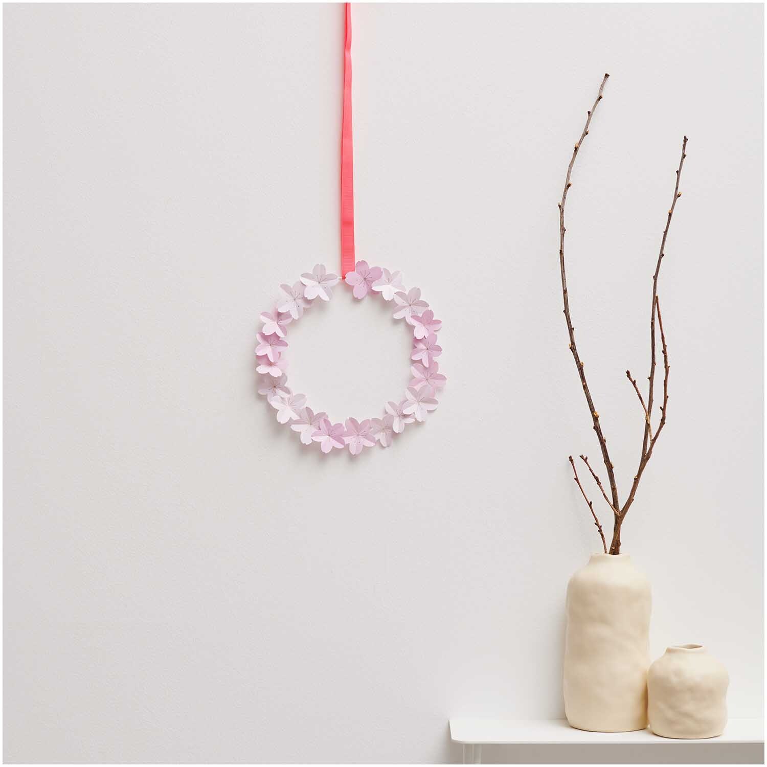 Metallring weiß matt von Rico Design, dekoriert mit rosa Blüten, hängt an rotem Band neben Vasen auf weißem Regal.