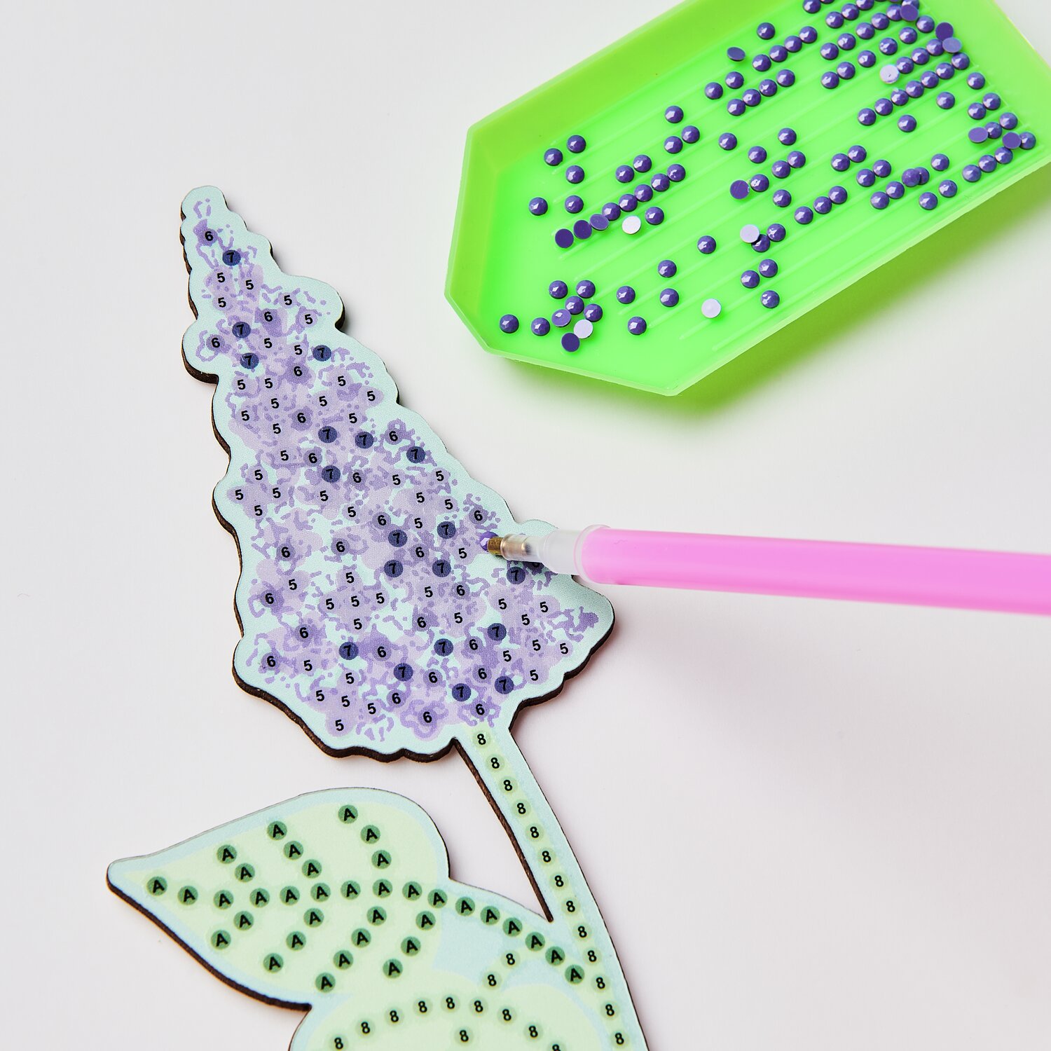 Diamond Painting DIY-Set Frühlingswiese 31x18,5cm: Rosa Stift platziert bunte Steine auf Blumenmotiv.