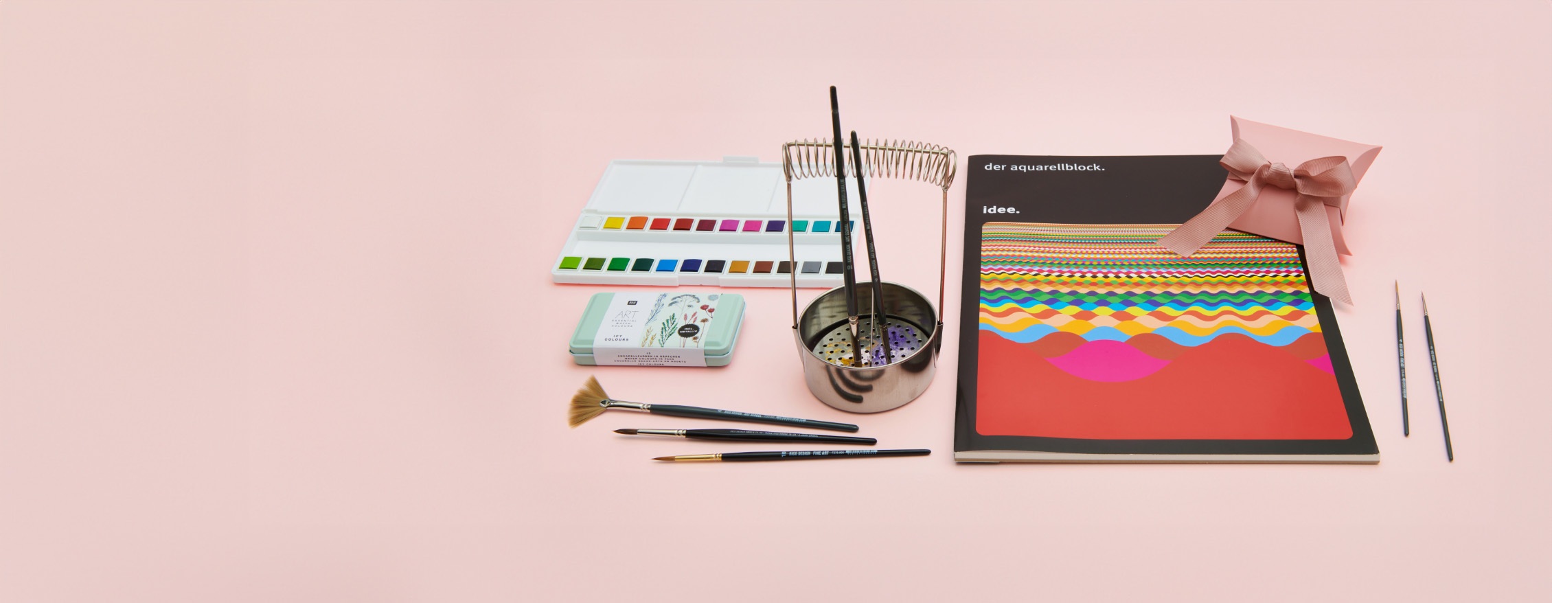 Verschiedene Materialien zum Aquarell malen. Ein Aquarellblock mit Aquarellfarbkasten, Pinseln und Pinselwascher. Fotosetting rosa Hintergrund.
