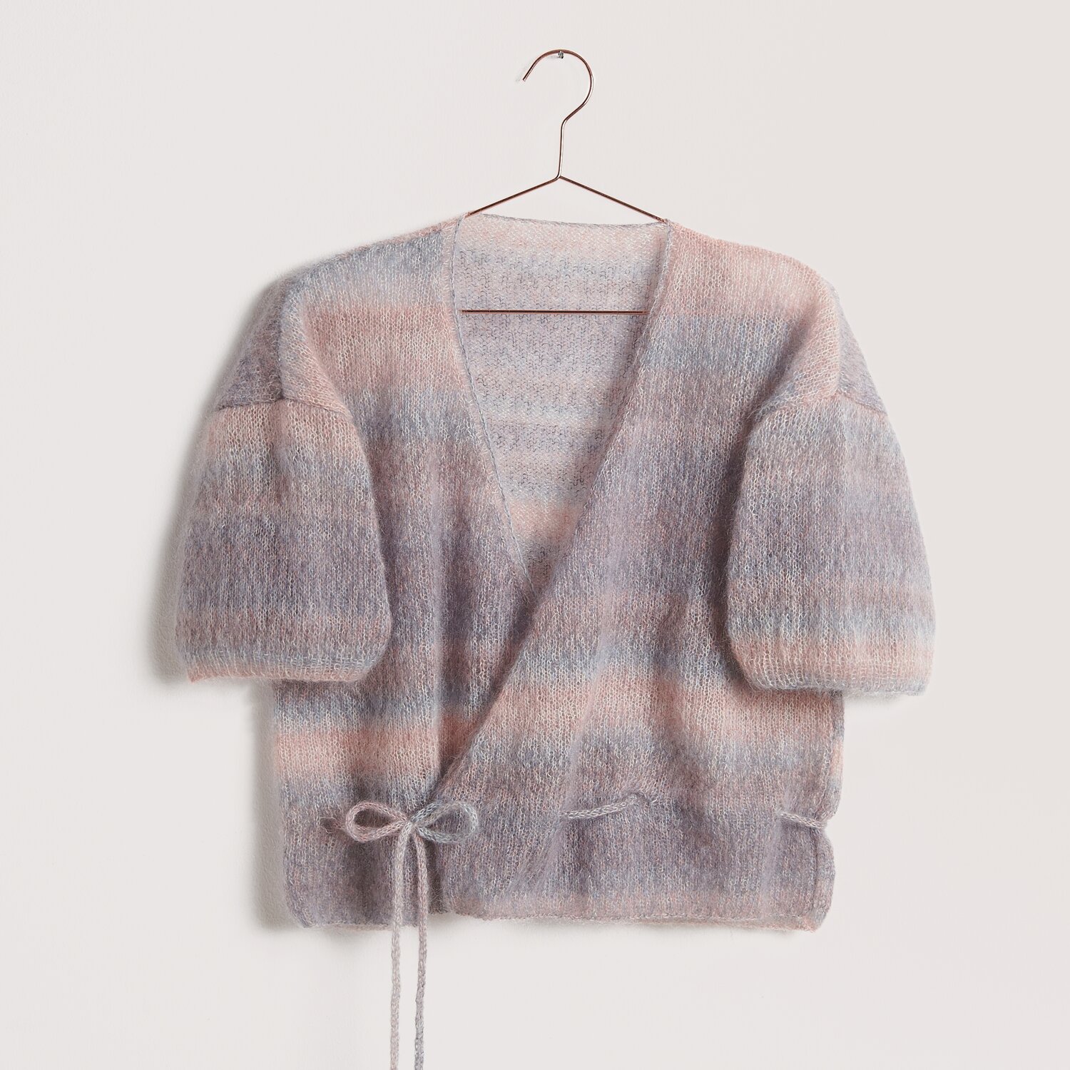 Die Neue Masche No. 12 Frühjahr-Sommer von idee. Creativmarkt Die Neue Masche No. 12: Weiche Strickjacke aus Super Kid Mohair in Pastelltönen, auf einem Bügel.