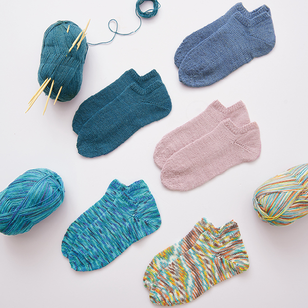 Fünf Paar gehäkelte Socken mit dem dazugehörigen Garn und Nadeln. Flatlay von Produkten.