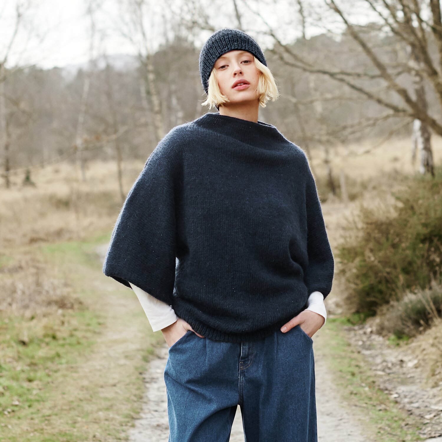 Strickset Pullover Modell 28 aus Lovewool No. 21 von Rico Design Strickset Pullover Modell 28 aus Lovewool No. 21: Frau in blauem Pullover und Mütze in Naturkulisse.