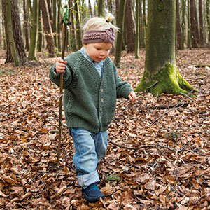 Kind läuft durchs Laub und trägt Strickjacke und Stirnband. Kind im Wald mit gestrickten Outfit