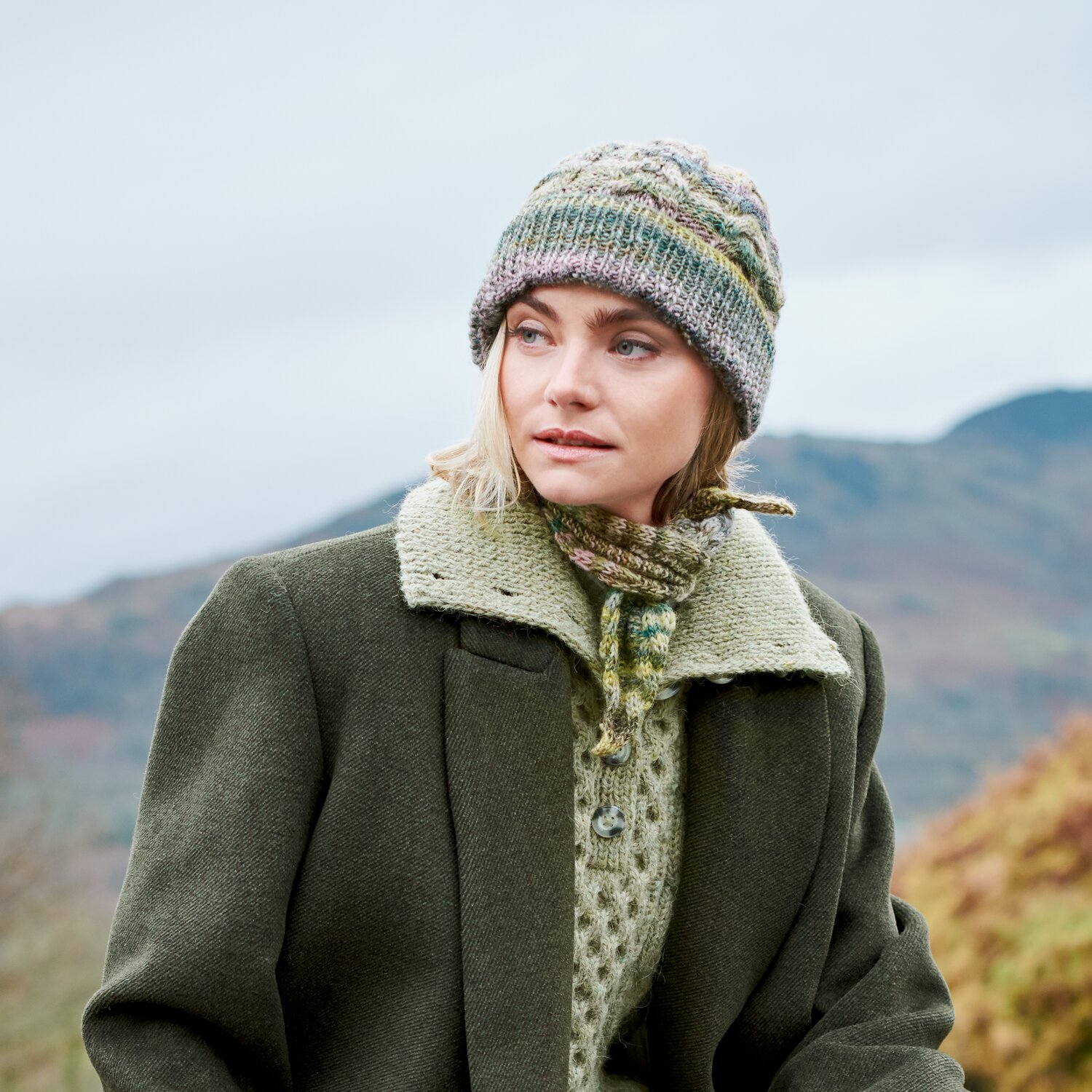 Strickset Mütze + Minituch Modell 07+08 aus Lovewool No. 23, getragen von Frau in Landschaft, mehrfarbig melierte Strickstrukturen, passender Schal zur wärmenden Jacke