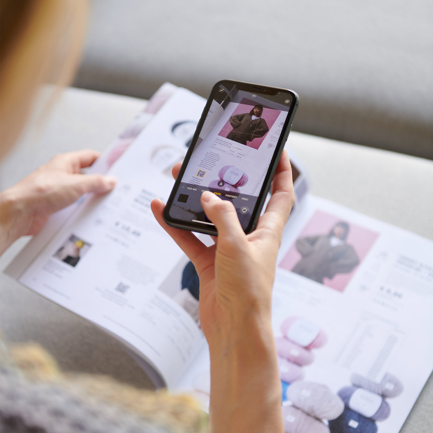 Hände halten einen Wolle Katalog in der Hand und scannen mit einem Handy einen QR-Code.