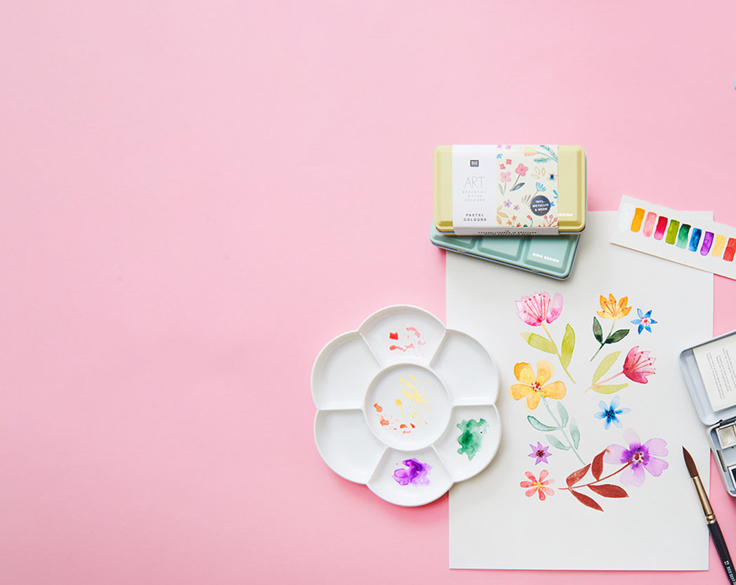 Ein Blumenbild mit Aquarellfarben gemalt, daneben zwei Aquarellfarbkästen und eine Malpalette. Flatlay von Produkten.