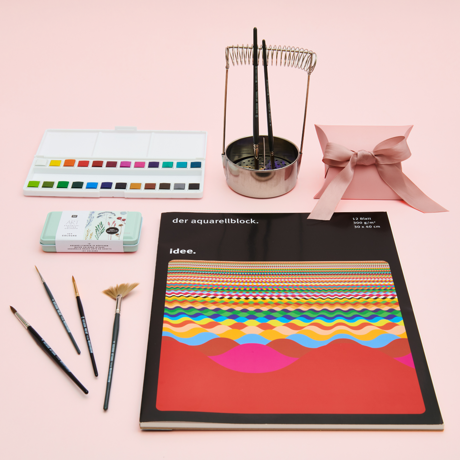 Ein Aquarellblock mit Aquarellfarbkasten, Pinseln und Pinselwascher. Fotosetting rosa Hintergrund.