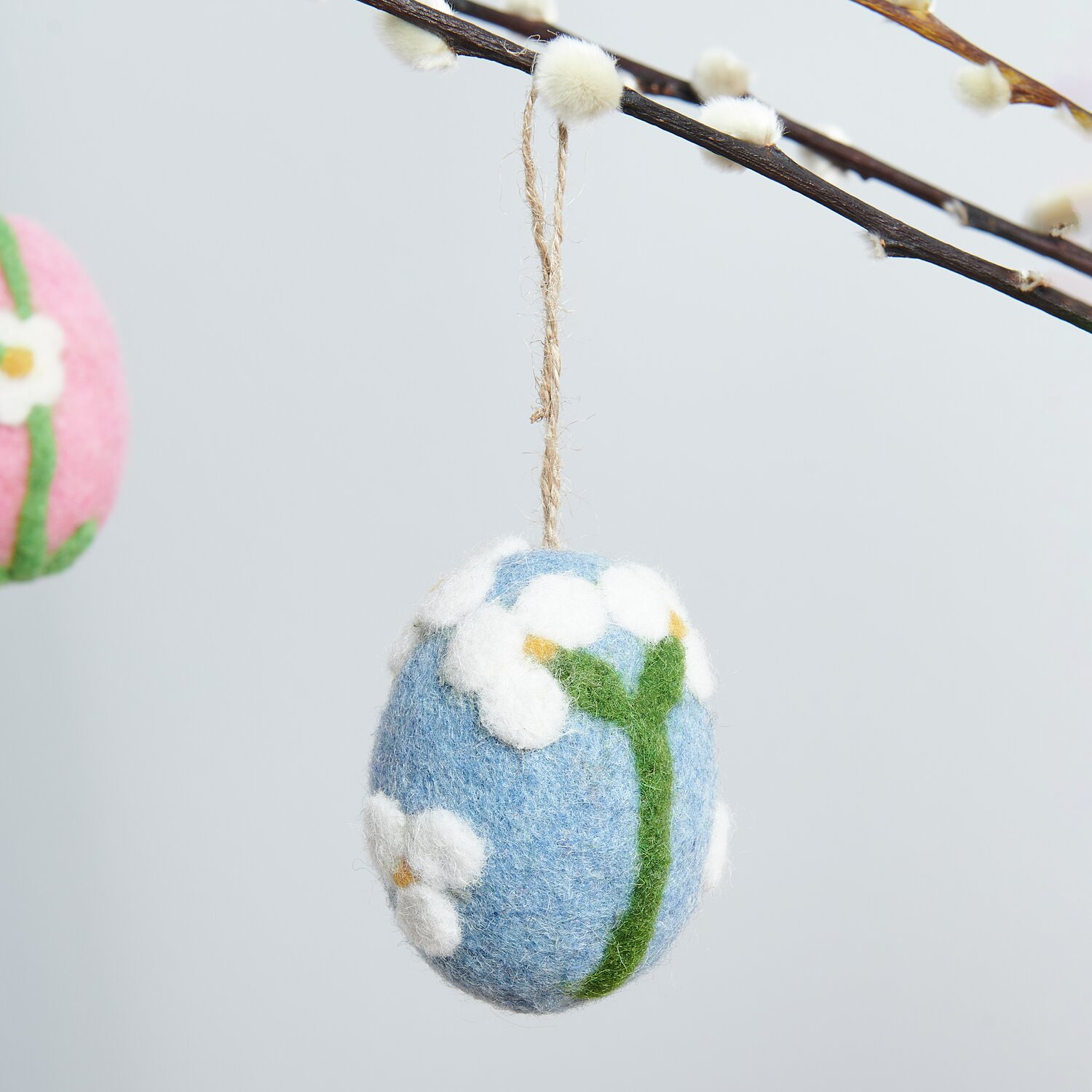 Aufhänger Filz-Ei Apfelblüte: Blaues Filz-Ei mit weißen Blüten, dekorativ an einem Ast hängend. Größe 7,8xØ5,8cm.