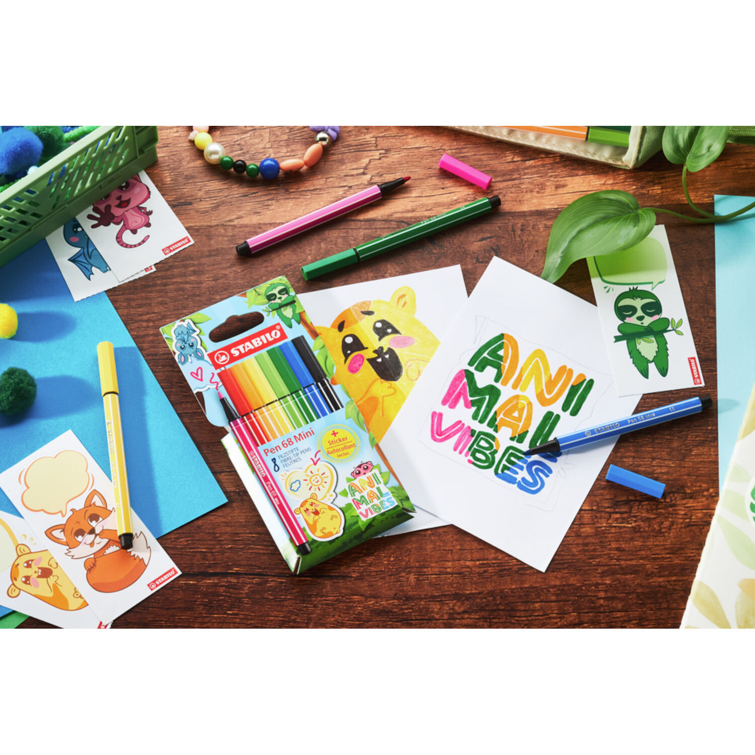 STABILO Pen 68 Mini Animal Vibes Set 8 Stück, bunte Filzstifte im Etui auf Holztisch, umgeben von Zeichnungen mit Tiermotiven und Schriftzug „Animal Vibes“