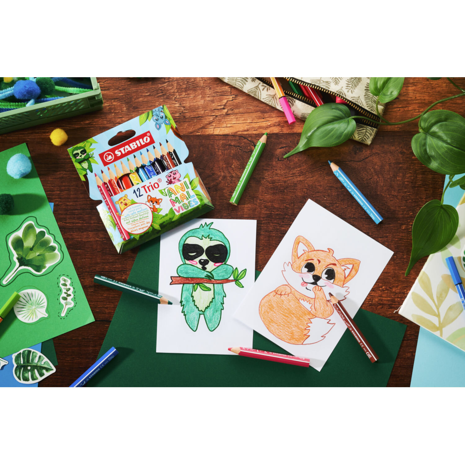 STABILO Trio Buntstifte Animal Vibes Set 12 Stück auf Holztisch mit farbigen Stiften, Verpackung und zwei gezeichneten Tiermotiven Fuchs und Faultier