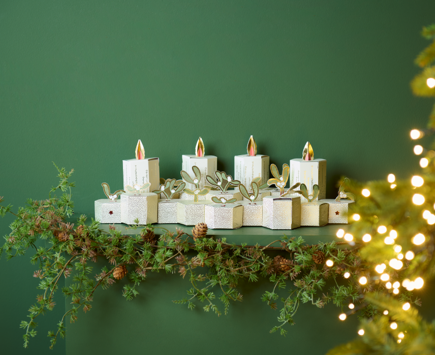 Adventskalender in  Kerzenformaus Papier mit Tannenzweigen und Lichterdekoration auf einem Regal.
