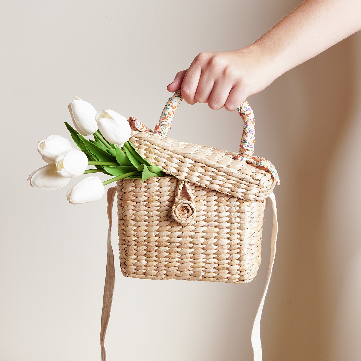 Tulpenstrauß mit 7 Blüten in einer handgehaltenen, geflochtenen Tasche. Die weißen Tulpen kontrastieren elegant mit dem natürlichen Material.