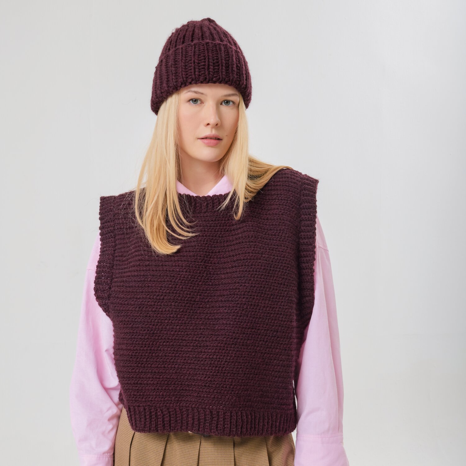 Häkelset Pullunder Modell 27 aus Made by Me No. 21 von Rico Design Häkelset Pullunder Modell 27 aus Made by Me No. 21: Frau trägt weinroten Pullunder und Mütze über rosa Hemd.
