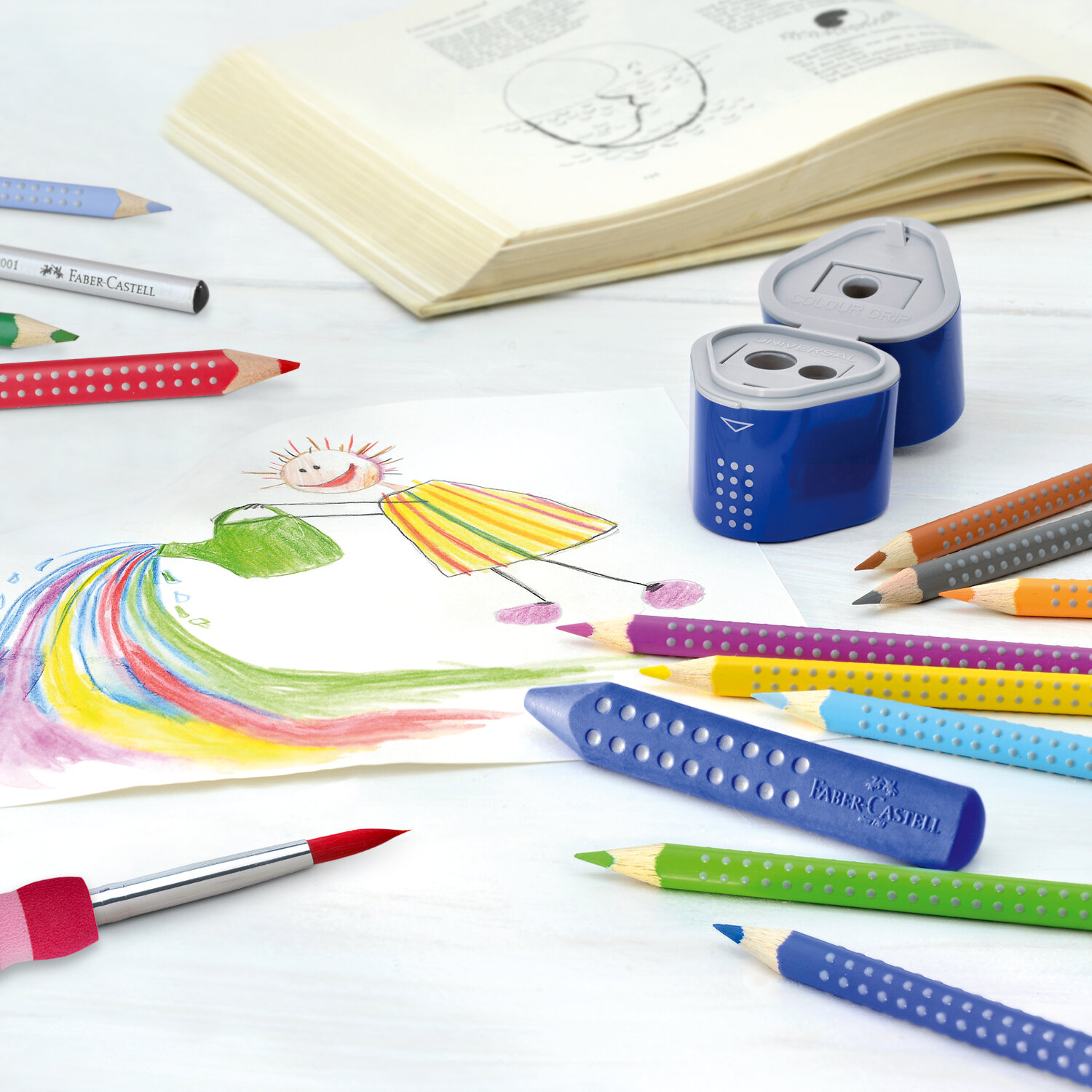 Colour Grip 2001: Buntstifte und Anspitzer von Faber Castell auf einem Tisch mit einer Kinderzeichnung.