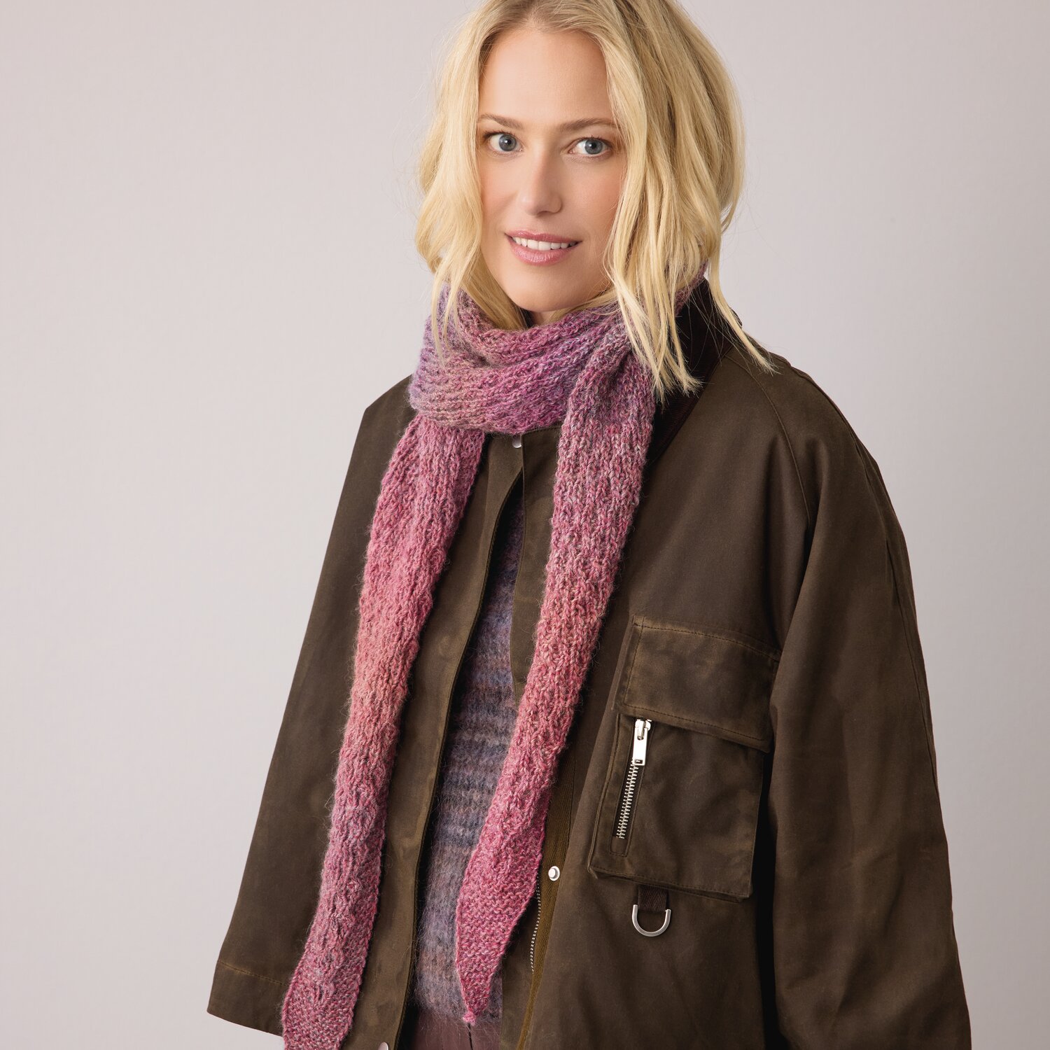 Strickset Dreieckstuch Modell 06 aus Die Neue Masche No. 14 von idee. Creativmarkt Strickset Dreieckstuch Modell 06 aus DNM 14: Frau trägt rosa Tuch über brauner Jacke.