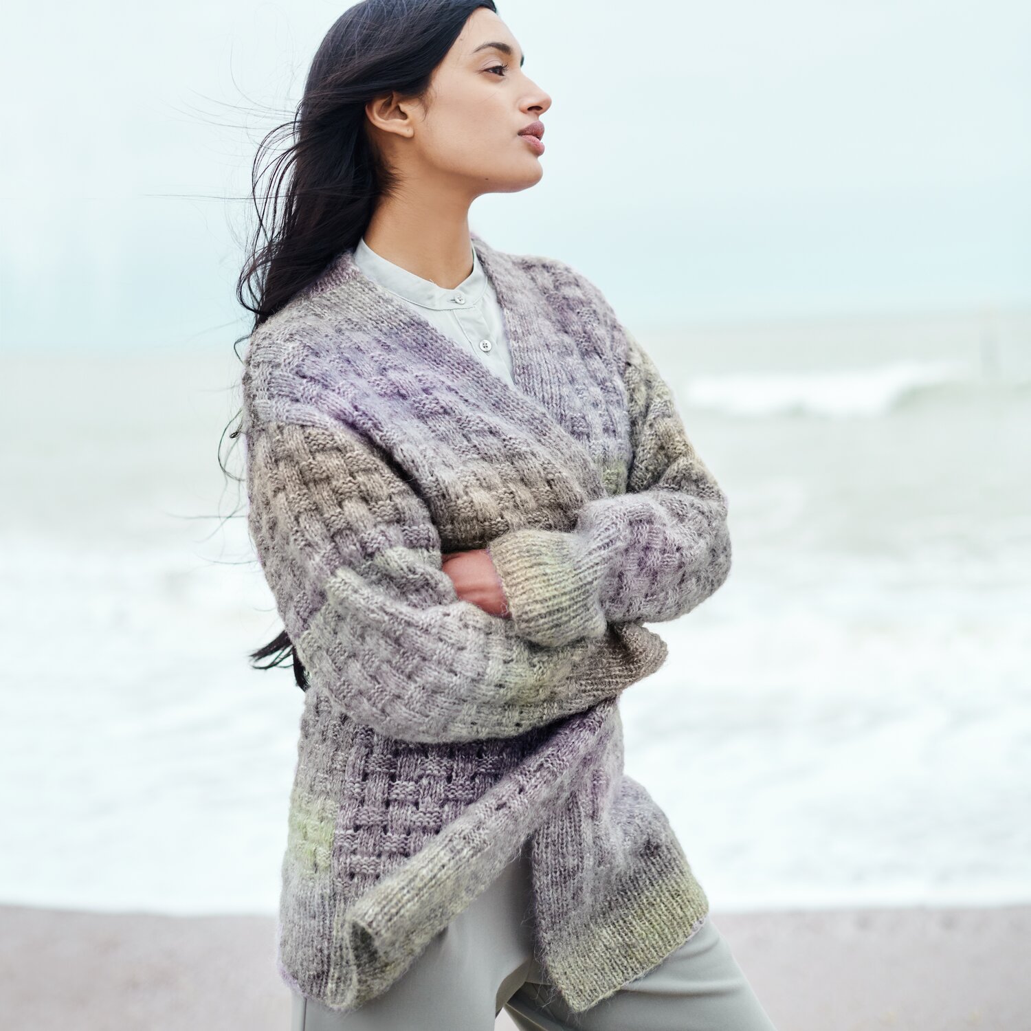 Strickset Cardigan Modell 21 aus Lovewool No. 21 von Rico Design Strickset Cardigan Modell 21 aus Lovewool No. 21: Frau am Strand in einem gestrickten, mehrfarbigen Cardigan.