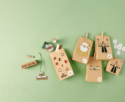 Blockbodenbeutel mit weihnachtlichen Stickern verziert, daneben Stempel, Geschenkanhänger und Washi Tape. Flatlay von Produkten.